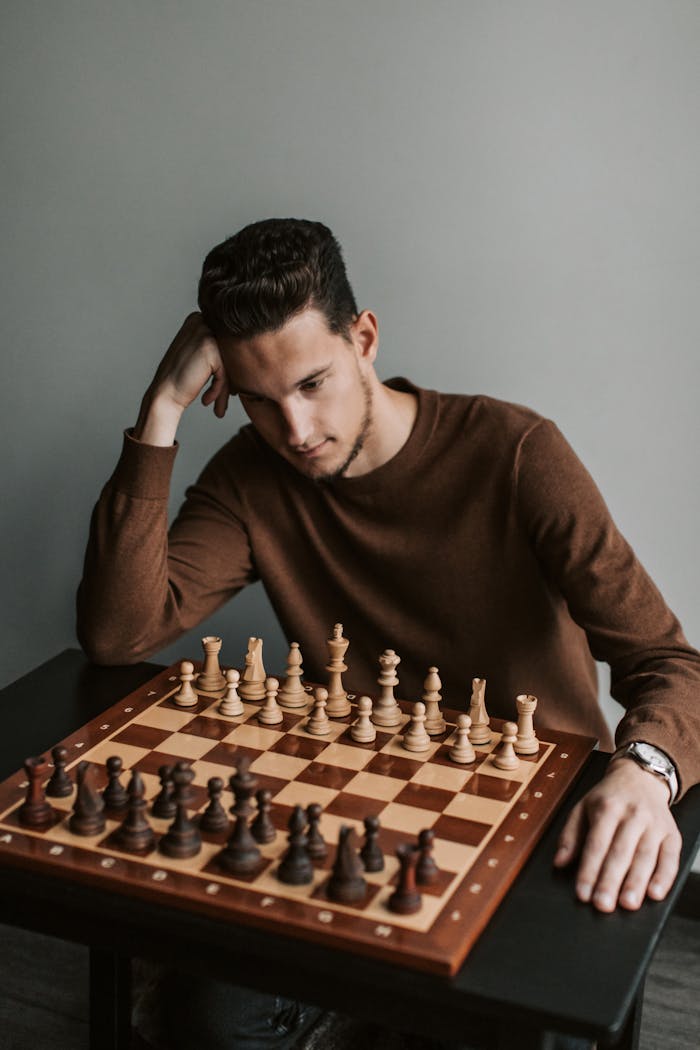 Man in brown sweater deeply focused on chess game strategy.